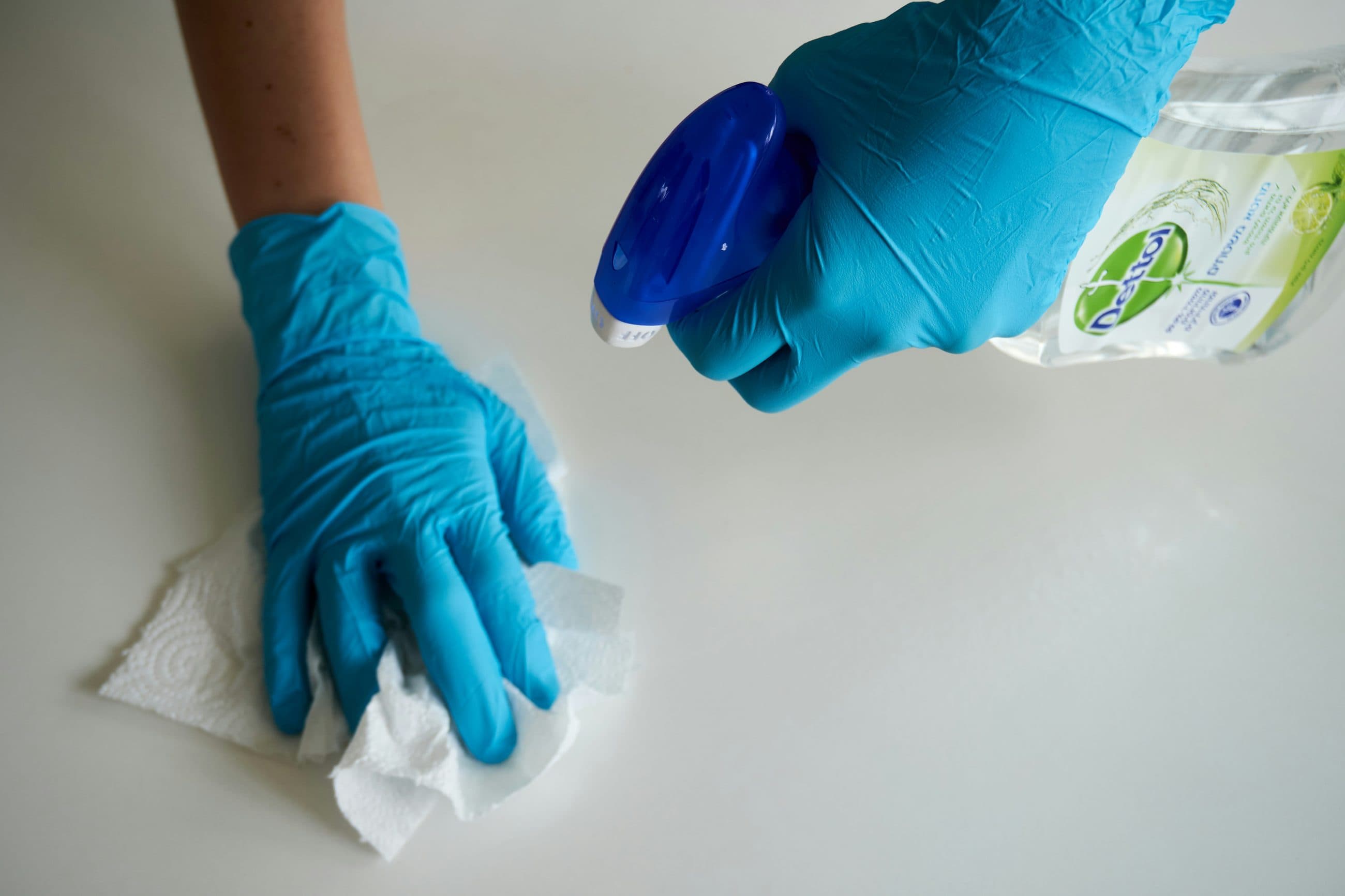 Gloved hands wiping down and sanitising a work surface