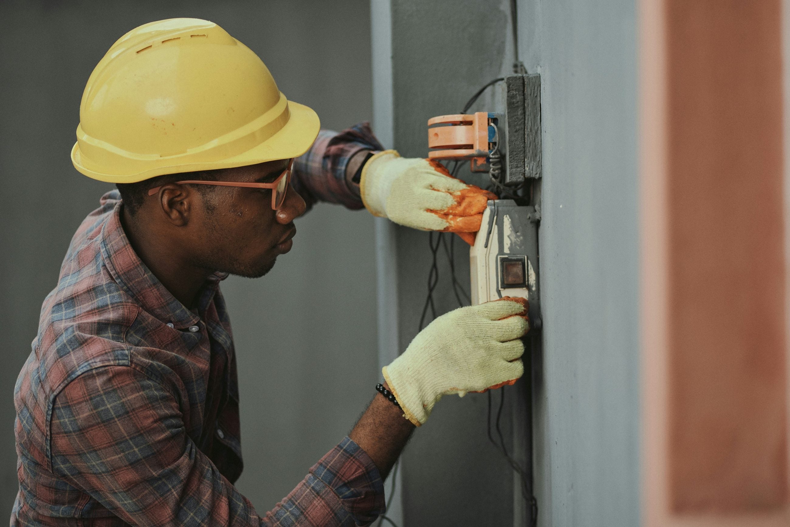 Electrician testing a wall-mounted junction box in protective gear